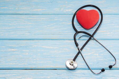A heart with a stethoscope lies on a light wooden background. Healthy heart