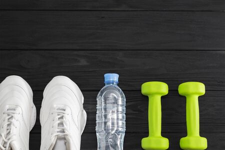 running shoes with dumbbells and a bottle of water on a black background. Healthy lifestyle.