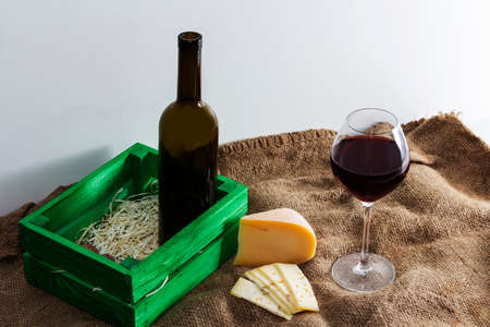 A bottle of red wine with a glass and a piece of cheese.の写真素材