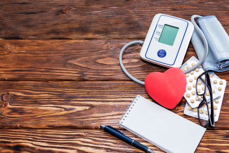 White electric tonometer, red heart and pills, on a brown wooden table