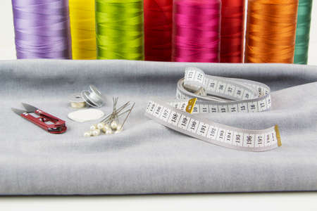 Colorful sewing threads, tailors scissors and measuring tape in the foreground.