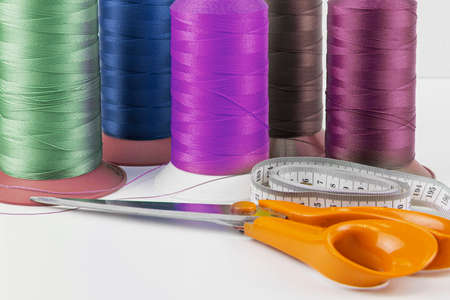 Colorful sewing threads, tailors scissors and measuring tape in the foreground.
