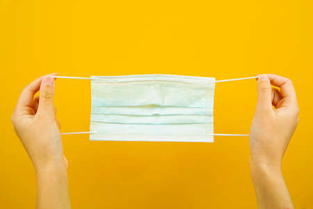 A hand holding a medical protective mask on a yellow background. Virus protection. An epidemic.