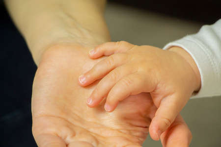 A woman's hand holding a newborn baby's hand.
