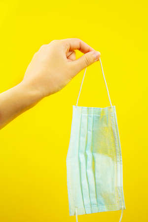 A hand holding a medical protective mask on a yellow background. Virus protection. An epidemicの写真素材