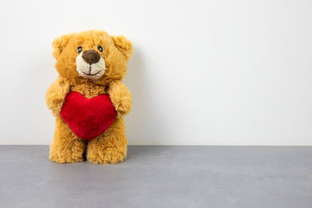 a teddy bear doll holding a heart-shaped pillow with love.の写真素材