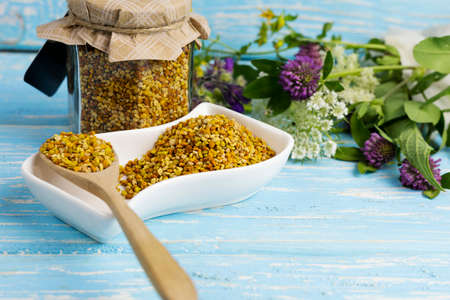 raw organic bee pollen on a wooden board surrounded by wildflowers.