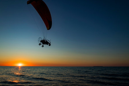 A person is joyfully parasailing high above the ocean during sunsetの写真素材