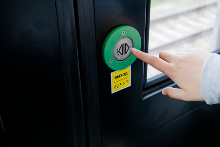 An individual is pressing a vibrant green button located on a door that likely serves as an entry...