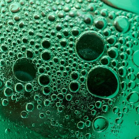 Drops of oil in the water close-up on a green background.の写真素材