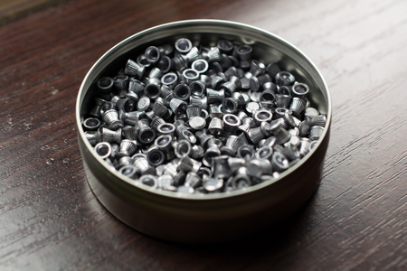 Small bullets for an air rifle in a round box. Box is on a wooden table. Small depth of field.の写真素材