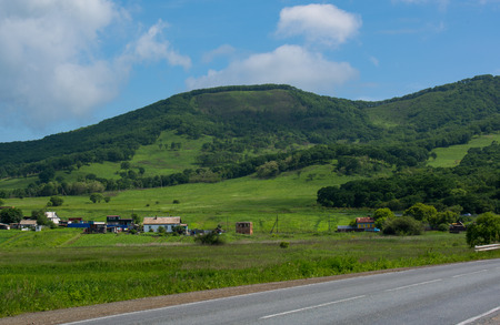 In the field of the road, there are houses near the foot of the mountainの写真素材