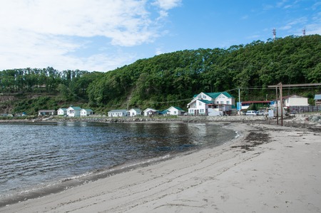 Beach huts on the sea shore under the green hill. Calm sea in summer day.の写真素材