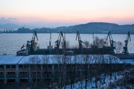 Morning View Of Winter Sea Port. Row Of Cranes Against Sea Vessel Near Pier. Sunrise Above Gulfの写真素材