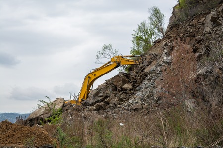 Part of excavator behind the slope. Yellow hydraulic bucket.の写真素材