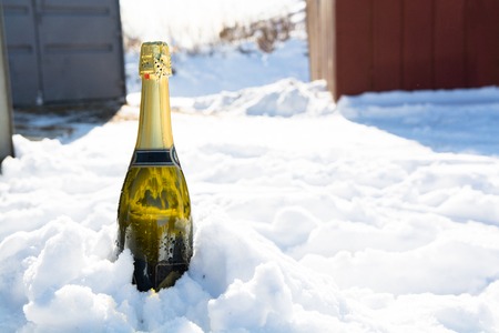 Bottle of champagne is sticking out from snow. Sunny winter day.の写真素材