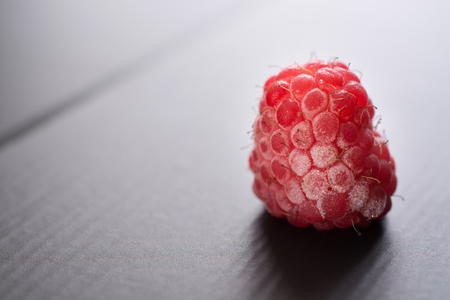 Frozen raspberry closeup. Berry on the black surface.