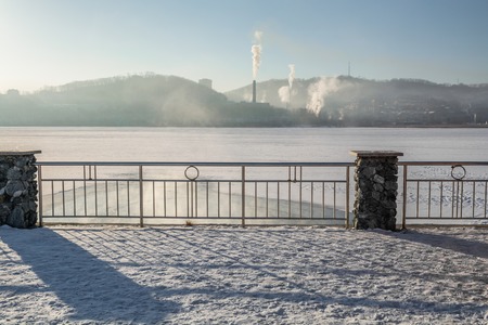 Bank of frozen lake and big steamshop's pipe on background. Smoke is rising up.の写真素材