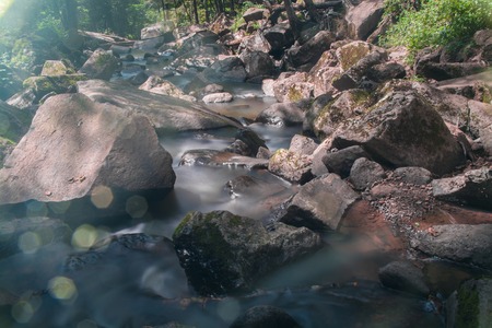 Stream flowing through big boulders. Shot on long exposure. The glare in the right corner.