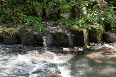 River bank with shaped edges formed by lava rocks. Water flow illuminated by summer sun.の写真素材