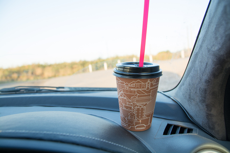 Coffee to go on the car dashboard. Cup made from cardboard with red tube for drinks.の写真素材
