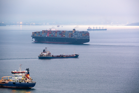 Few nautical ships in a harbor at early morning. Big container ship anchored in the sea bay.の写真素材