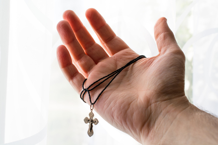 Metal cross in the hand with focus on the hand. Cross with black cord.の写真素材