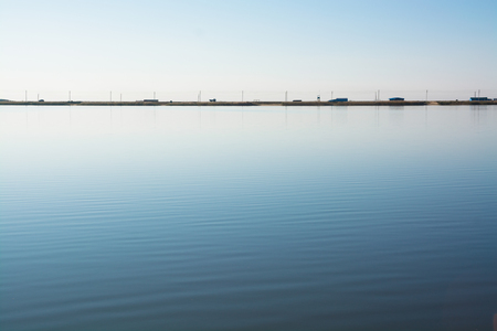 Minimalistic water landscape with road on the lake shore. Alone car moving in the distance.の写真素材