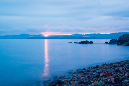 Orange sunset above hilly side of sea. Overcast sky and reflection on water.の写真素材