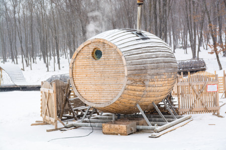 Unusual wooden sauna among snow. Bathhouse in shape of barrel. Snowy winter day.の写真素材