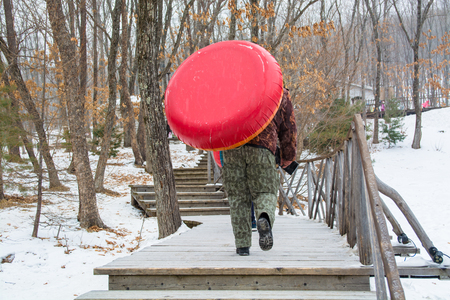 Man pulling up inflatable tubing up stair. Riding on icy hill.の写真素材