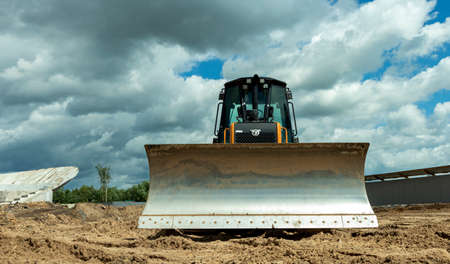 an orange bulldozer stands on a construction site with a lowered knife