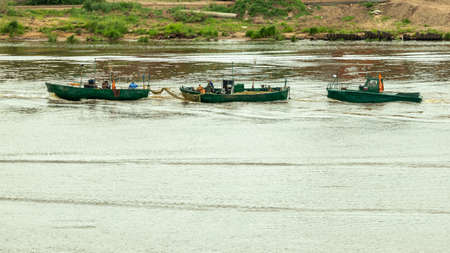 three green fishing boats float along the shore