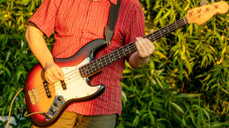 a man plays bass guitar in a park at sunset