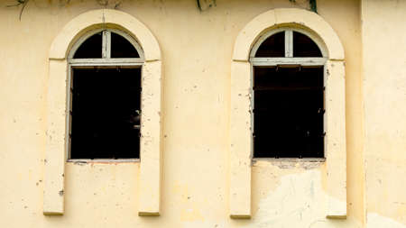 a yellow abandoned building with two damaged Windows