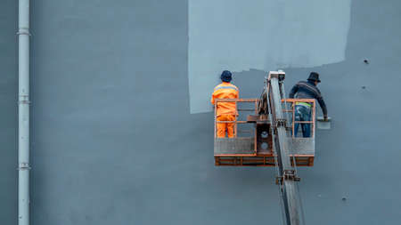 two builder painter in a construction cradle paint the facade of a buildingの写真素材