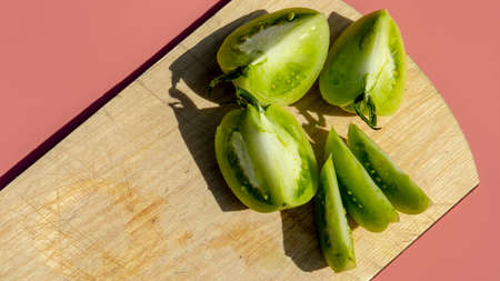 sliced green unripe tomato on pink background, isolated
