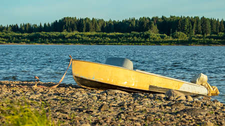 orange boat parked on a rocky shore, against a background of sky and forestの写真素材