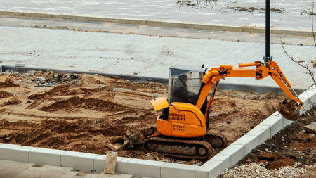 a small yellow excavator levels the ground on a playground for mounting a swingの写真素材