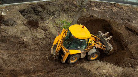 yellow construction excavator throws the earth onto a flower bed, an unusual angle