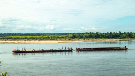A large river vessel pulls two barges loaded with timber down the river