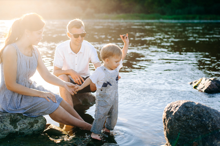 a small child with his parents walk by the river. child throws stones in a riverの写真素材