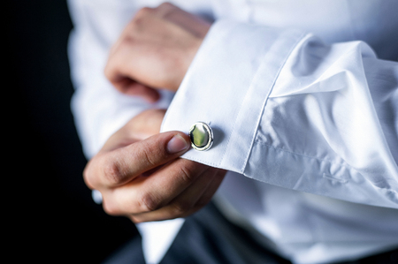 A man adjusts his cuff on a white shirt. The guy straightens the sleeve. Close-up of sleeves.の写真素材