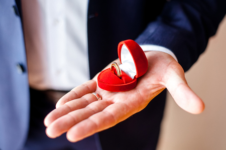 Wedding ring in a special box, holds in the hands of the groom. Man in a suit shows a ringの写真素材