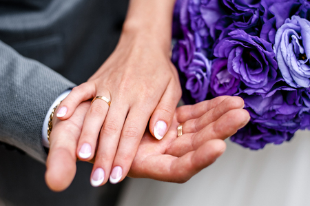 Hands of newlyweds with rings and a purple bouquet of flowers.The bride laid her hand on the groom's hand.の写真素材