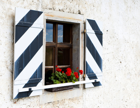 Old wooden window with shutters and red flowersの写真素材