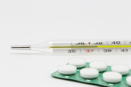 White Pills and a thermometer on white background