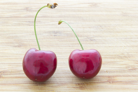 Two red cherries isolated on wooden backgrounの写真素材