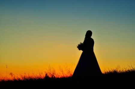 Silhouette of bride against a warm sunsetの写真素材