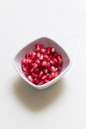 Pomegranate in a dipping bowl on simple white backgroundの写真素材